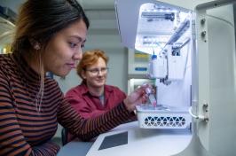 A male and female student work together in front of a piece of scientific equipment